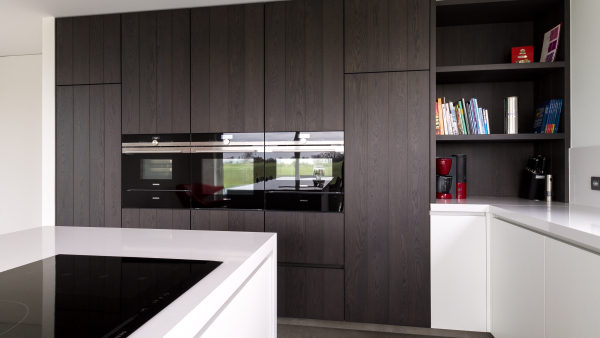 Moderne keuken met donkere houten kasten, geïntegreerde ovens en een stijlvol design dat warmte en functionaliteit combineert